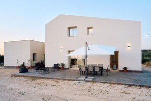 A modern two-story building with a patio area featuring outdoor seating and a large umbrella. - New Listing (Sicilia)
