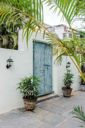 A white wall with a blue door, two potted plants, and two wall-mounted lights. - Staymaster White Castle - 7BHK Villa (Goa)
