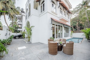 A white building with a pool, outdoor furniture, and palm trees. - Staymaster White Castle - 7BHK Villa (Goa)