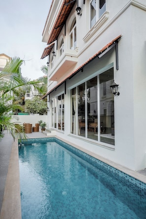 A two-story building with a swimming pool, large windows, and outdoor furniture. - Staymaster White Castle - 7BHK Villa (Goa)