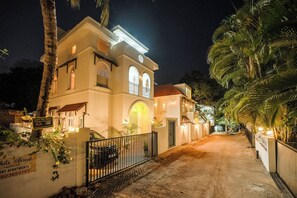 Un edificio de dos pisos con entrada protegida por un portón, un letrero que indica alquiler de coches y una fachada bien iluminada.