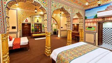 A room with a large bed, a desk, and a bench. There are ornate arches and a patterned ceiling.