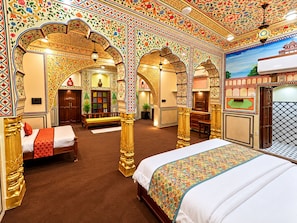 Ein Zimmer mit einem großen Bett, einem Schreibtisch und einer Bank. Es gibt kunstvolle Bögen und eine verzierte Decke.
