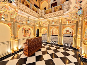 Una hall d'albergo con pavimento a scacchi, decorazioni murali elaborate e una panca di legno al centro.