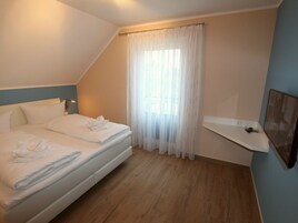 Habitación de hotel con cama, ventana con cortinas translúcidas, mesita de noche y estante montado en la pared.