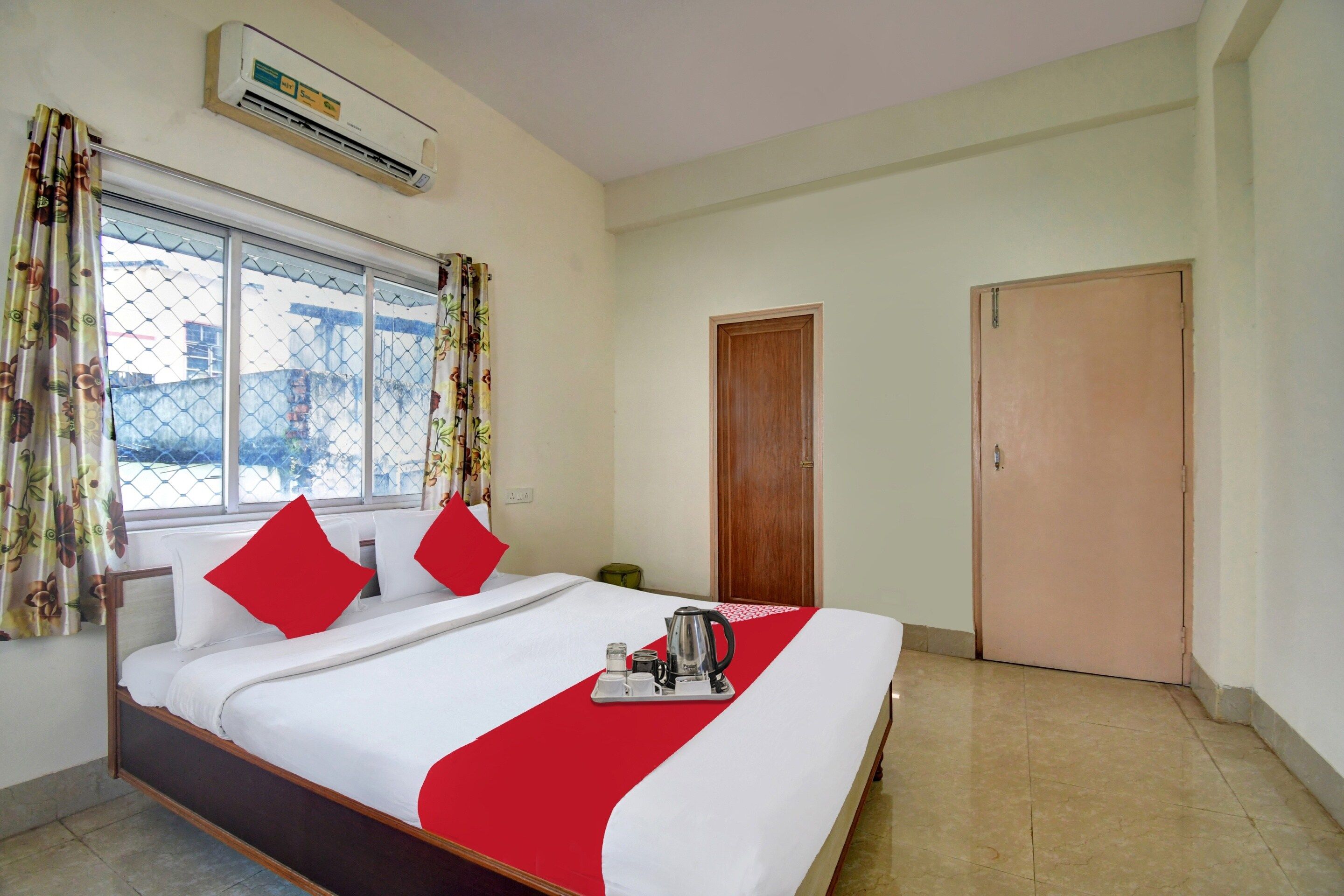 Una habitación de hotel con cama, ventana con cortinas, aire acondicionado y una puerta.