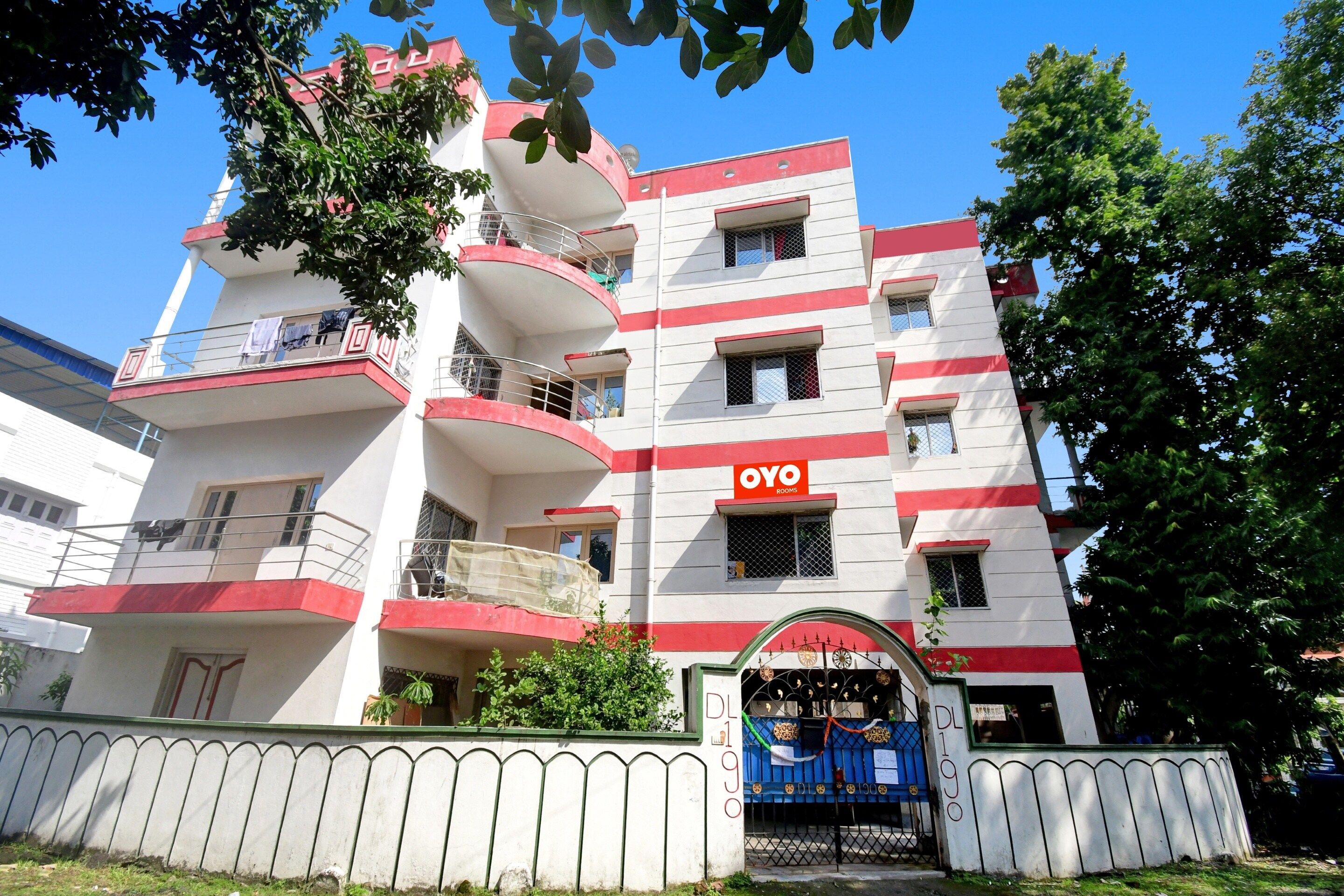 Un edificio de varios pisos con balcones, un letrero que dice 'OYO ROOMS' y una entrada con portón.