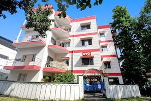 Un immeuble à plusieurs étages doté de balcons, une enseigne indiquant « OYO ROOMS », et une entrée fermée par un portail.
