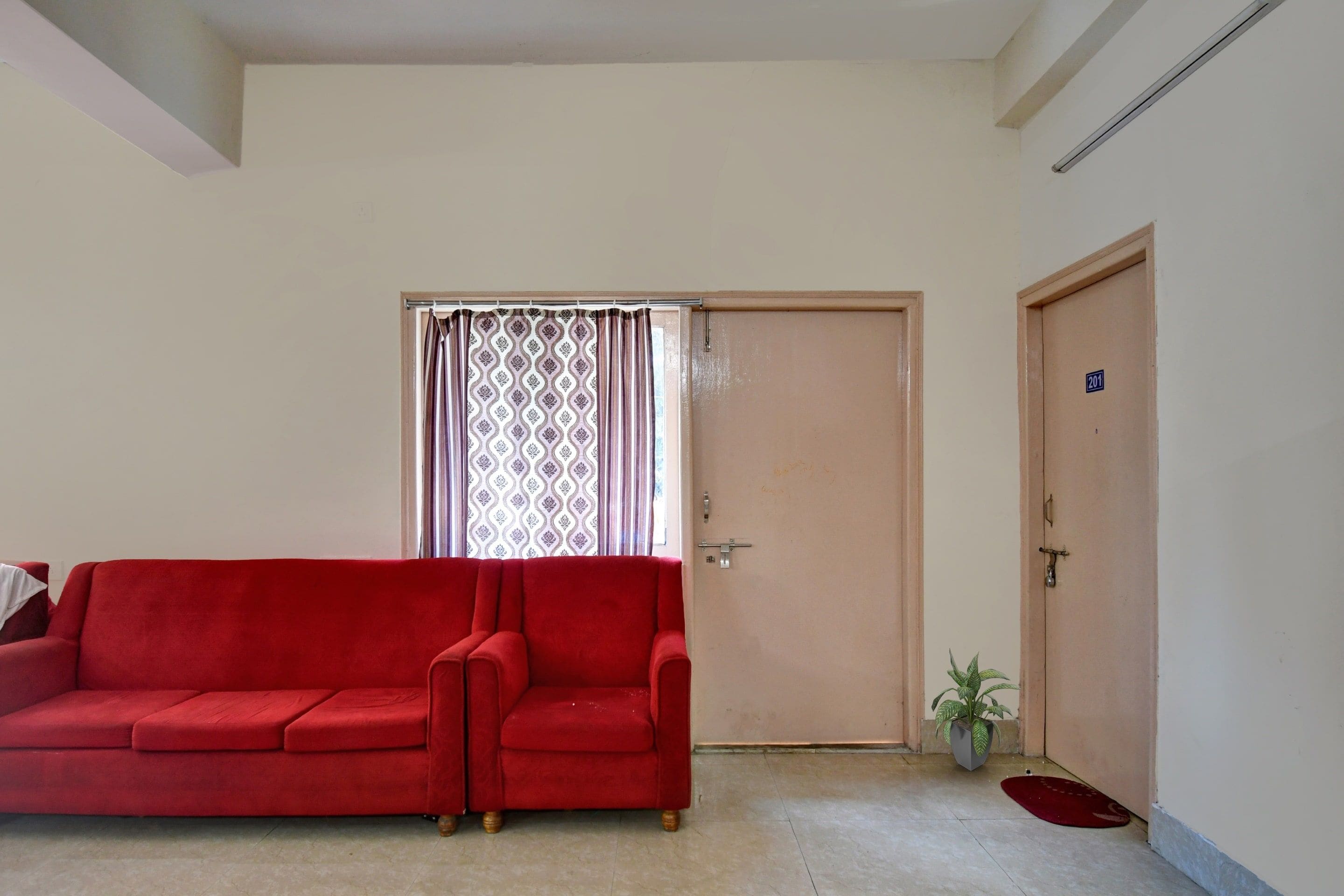 A red sofa in a room with a door marked '201' and a potted plant.