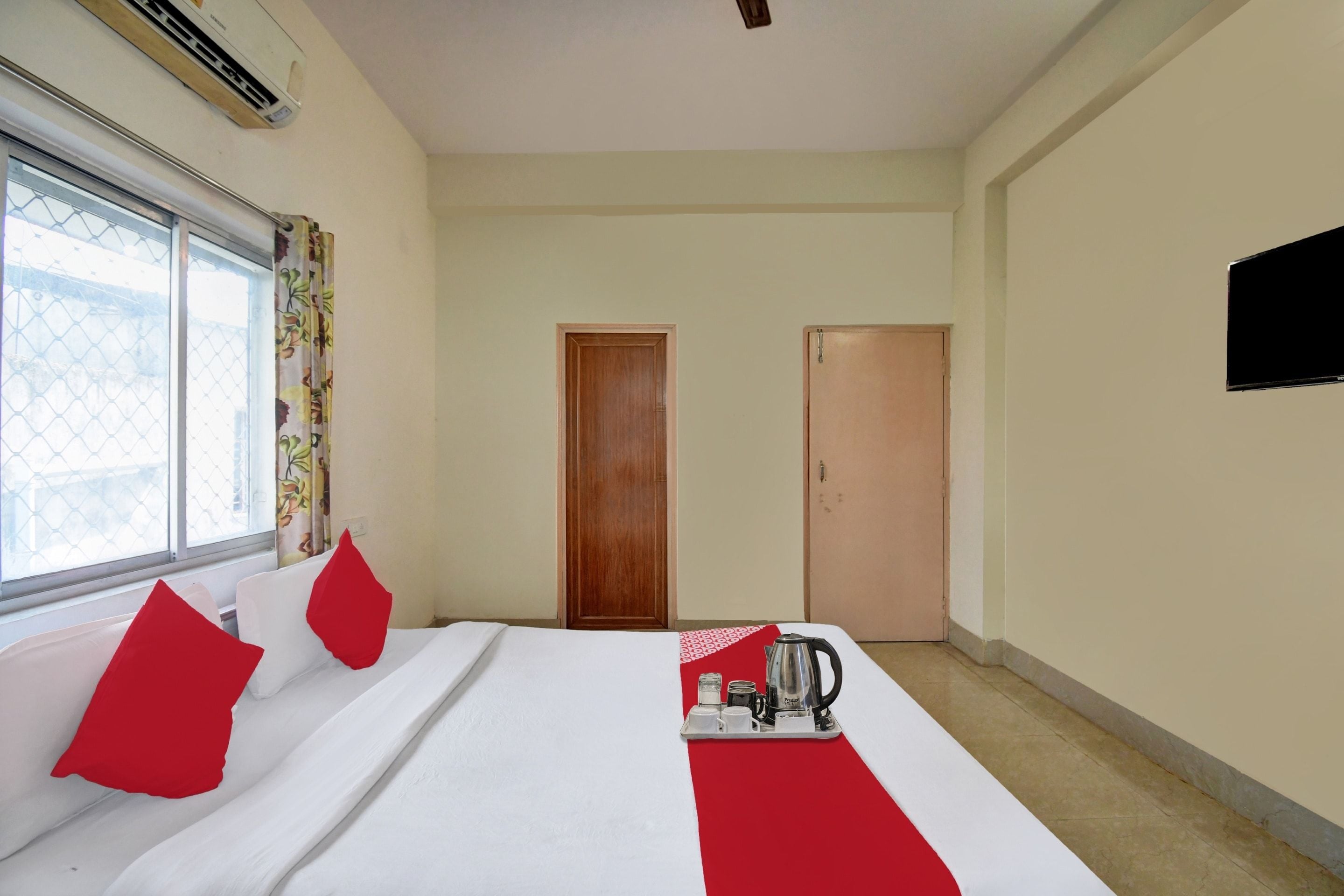 A hotel room with a bed, a window with curtains, a door, and a wall-mounted TV.