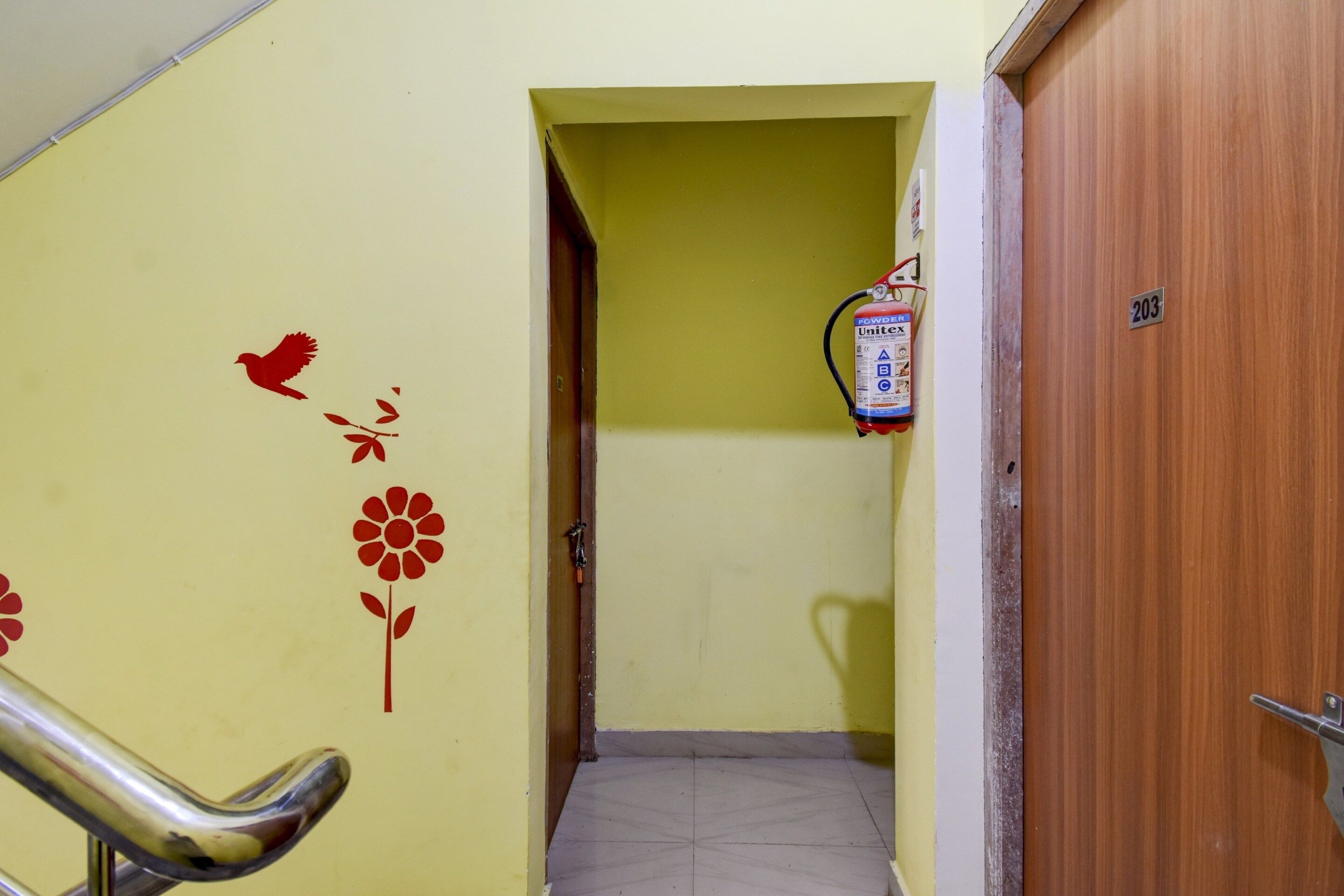 A hallway with a fire extinguisher mounted on the wall, a number sign, and a door.