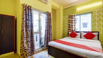 Habitación de hotel con cama, dos ventanas con cortinas estampadas, un armario y un equipo de aire acondicionado.