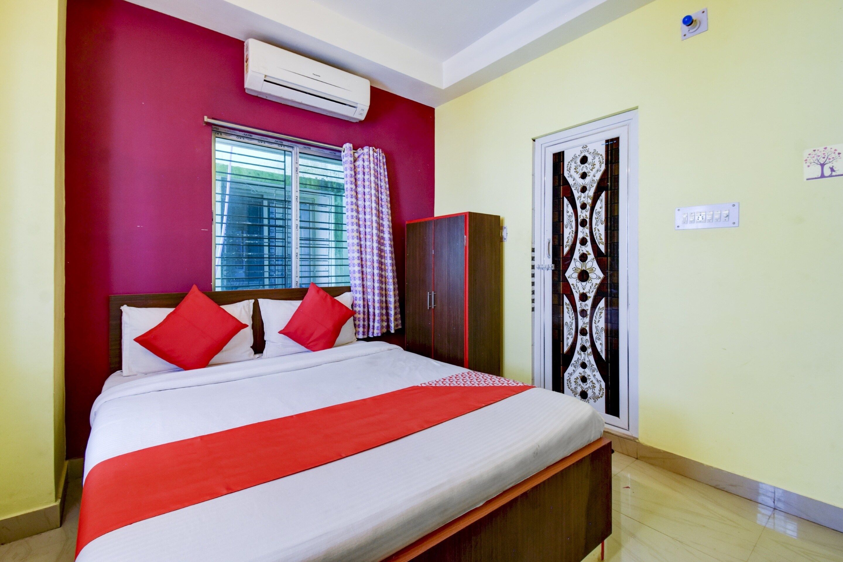 A bedroom with a bed, a wardrobe, a window with curtains, and an air conditioning unit.