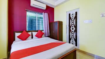 A bedroom with a bed, a wardrobe, a window with curtains, and an air conditioning unit.
