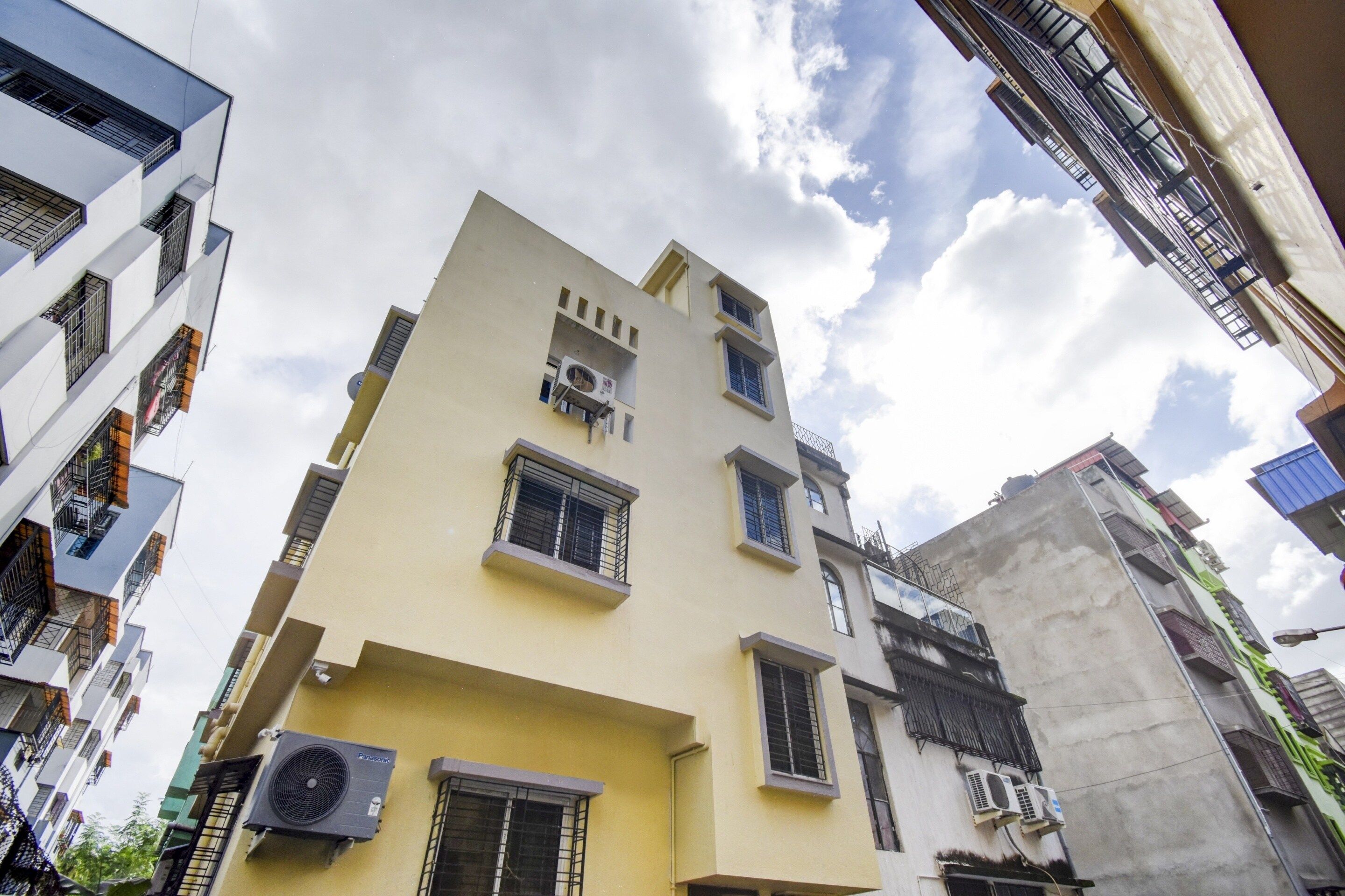 A multi-story building with air conditioning units, a balcony, and a window with a metal grille.