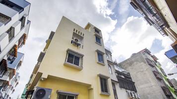 A multi-story building with air conditioning units, a balcony, and a window with a metal grille.