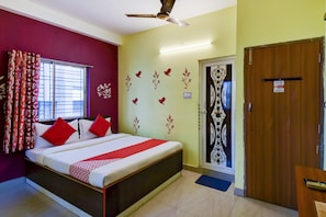 A hotel room with a bed, a window with curtains, a door with a decorative panel, and a ceiling fan. - Hotel O Ankita Guest House (Kolkata)