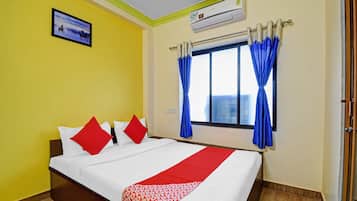 Habitación de hotel con cama, paredes amarillas, ventana con cortinas azules y un equipo de aire acondicionado.