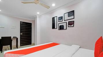 Habitación de hotel con cama, escritorio, silla, ventilador de techo y cuadros en la pared.