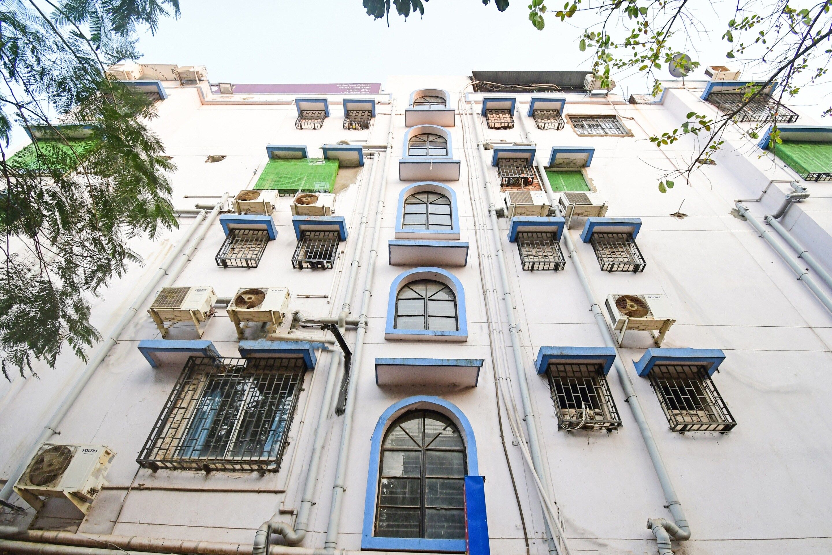A building with multiple windows, some with metal grilles, and air conditioning units attached to the exterior walls.