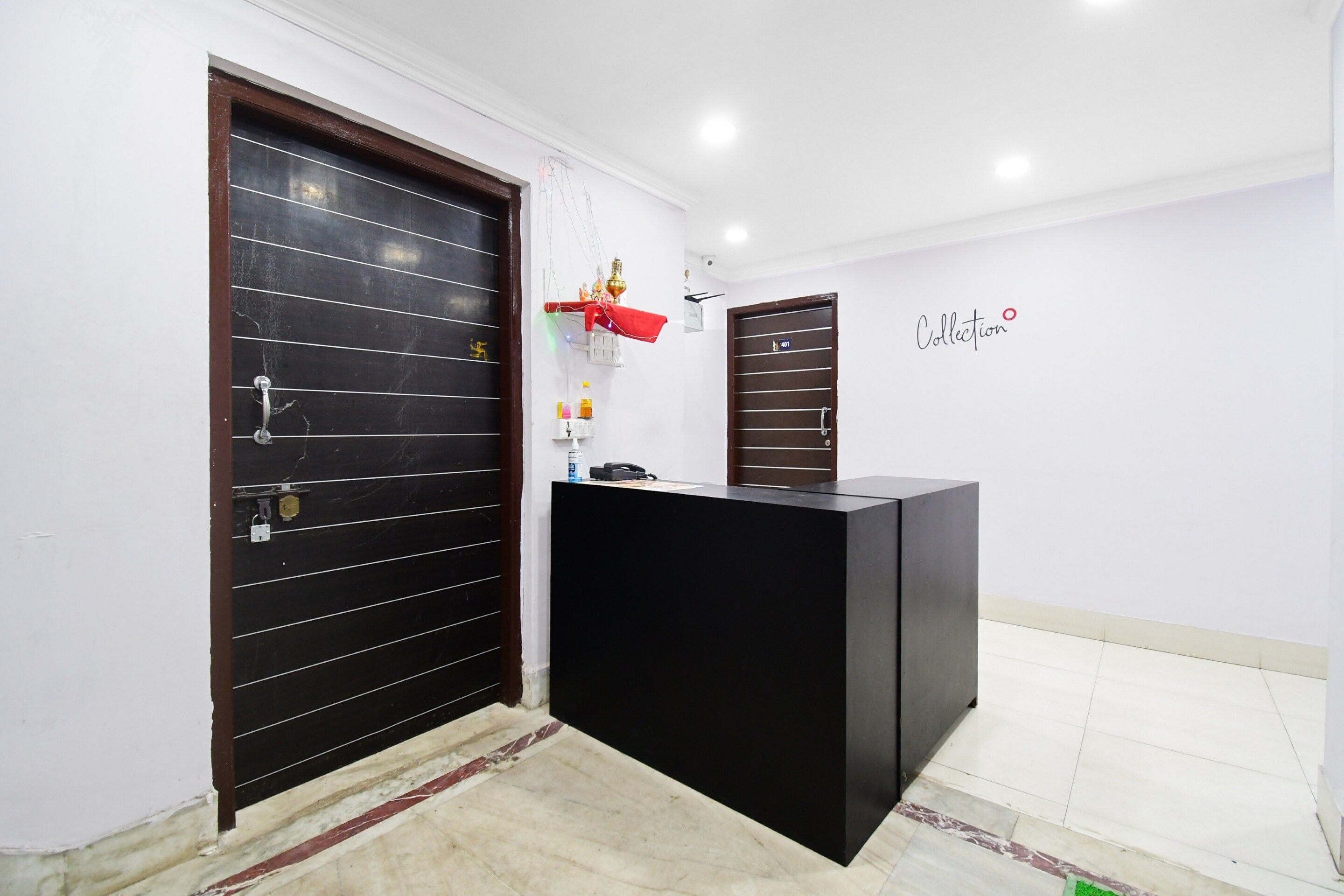 A reception area with a black reception desk, two dark wooden doors, a wall-mounted shelf with items, and a tiled floor.