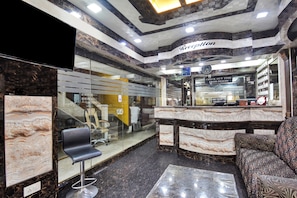 A reception area with a marble counter, a reception desk, a black office chair, and a patterned sofa. - Collection O Aafreen Tower Near St. (Kolkata)