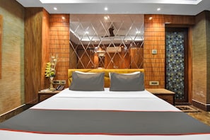 A hotel room with a large bed, a nightstand, a vase with flowers, and a patterned wall. - Collection O Aafreen Tower Near St. (Kolkata)