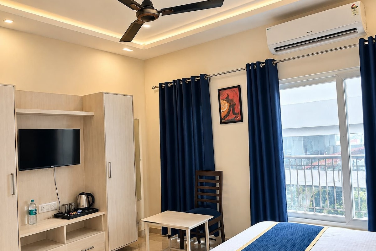 Una camera d'albergo con un letto, una scrivania, una sedia, una televisione, un armadio e una finestra con tende.