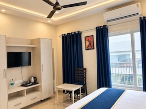 A hotel room with a bed, a desk, a chair, a TV, a wardrobe, and a window with curtains. - The Sapphire Inn Hotel (Haldwani)