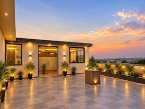 A modern building with a glass entrance, potted plants, and a view of the cityscape at sunset. - The Sapphire Inn Hotel (Haldwani)