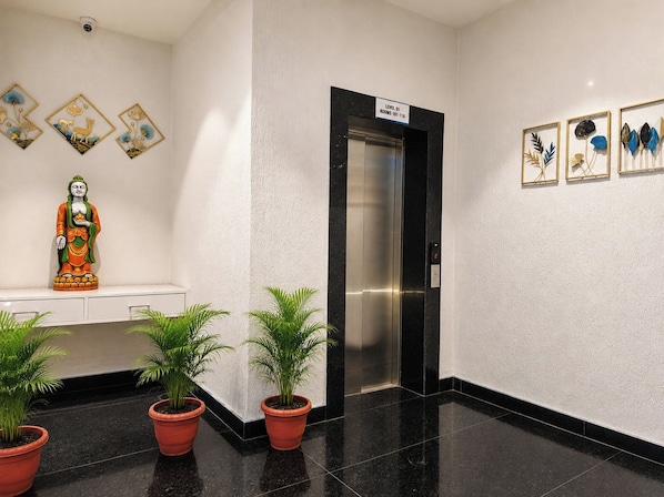 A modern elevator with a digital display, a statue, and framed artwork on the walls. - The Sapphire Inn Hotel (Haldwani)