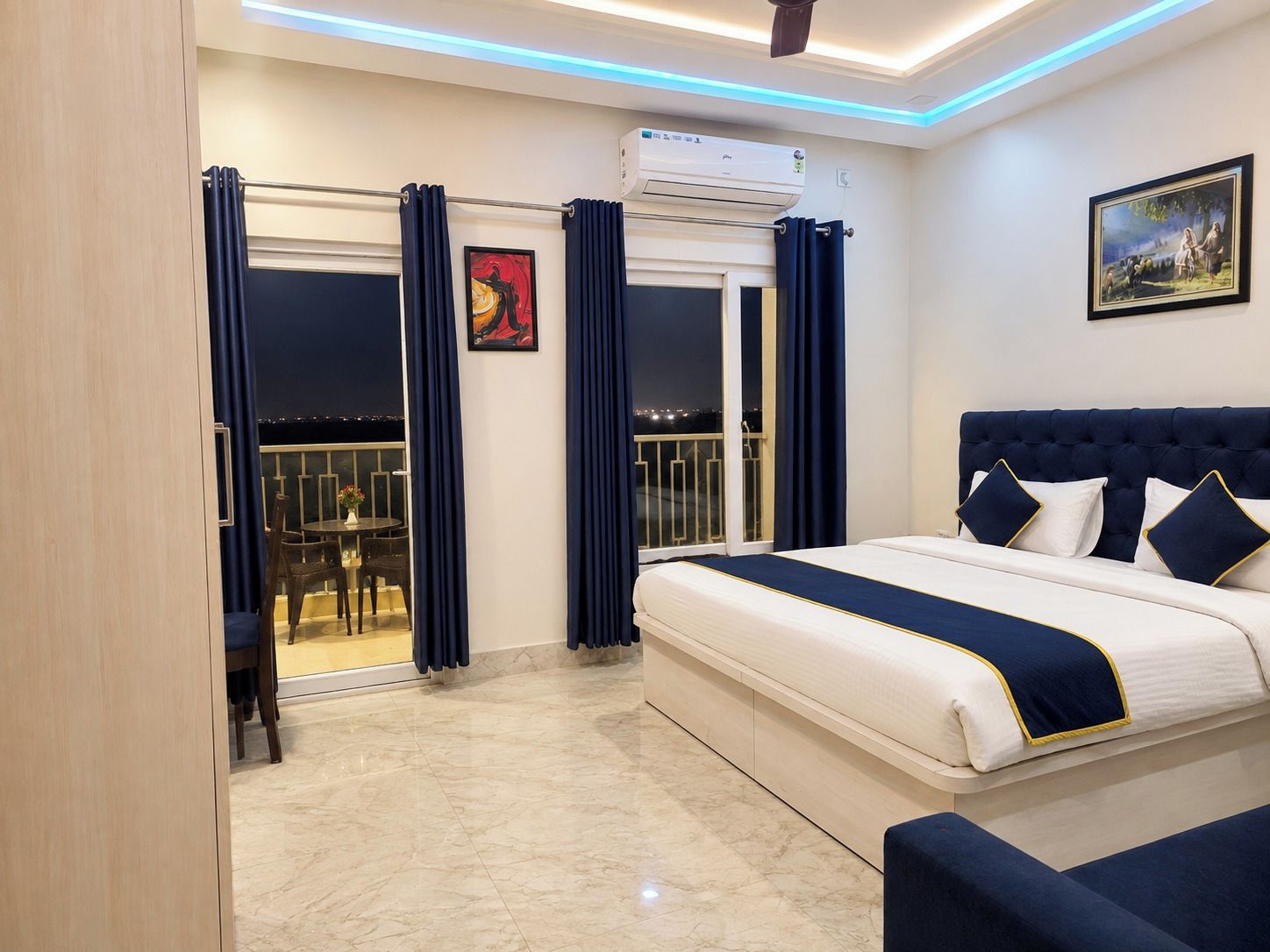 Una habitación de hotel con cama, un balcón con cortinas, un equipo de aire acondicionado y un cuadro en la pared.