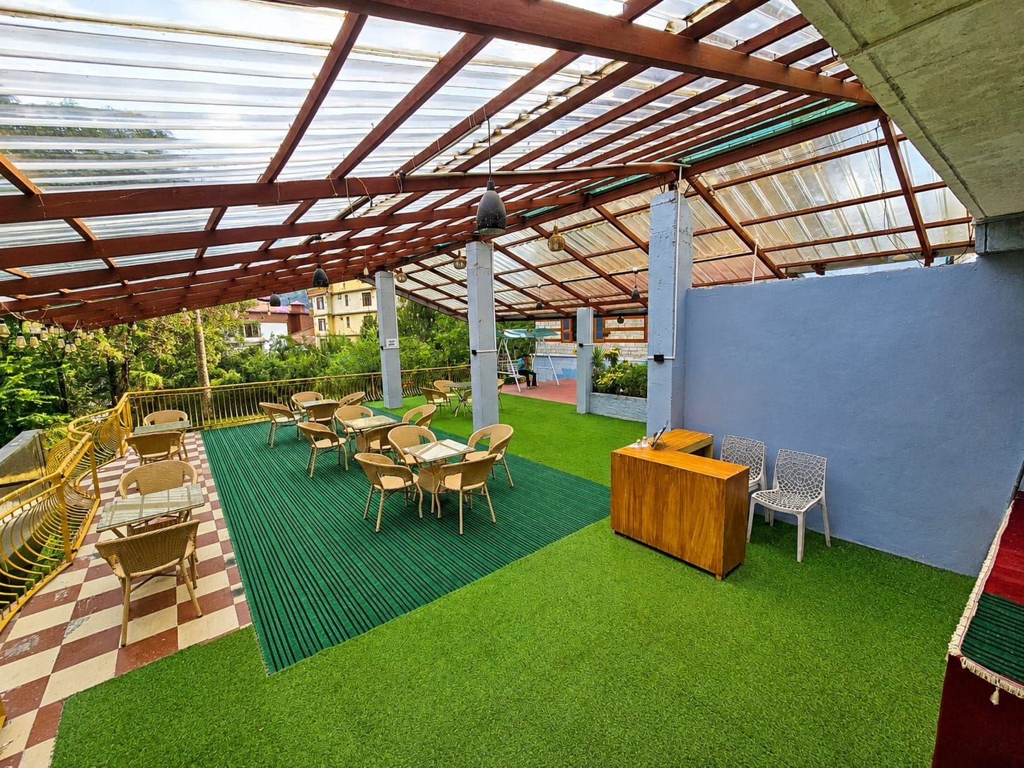 An outdoor patio with artificial grass, wooden tables and chairs, and a wooden reception desk.