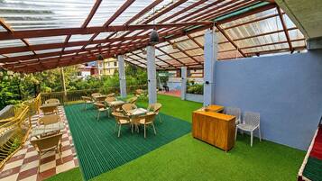 An outdoor patio with artificial grass, wooden tables and chairs, and a wooden reception desk.
