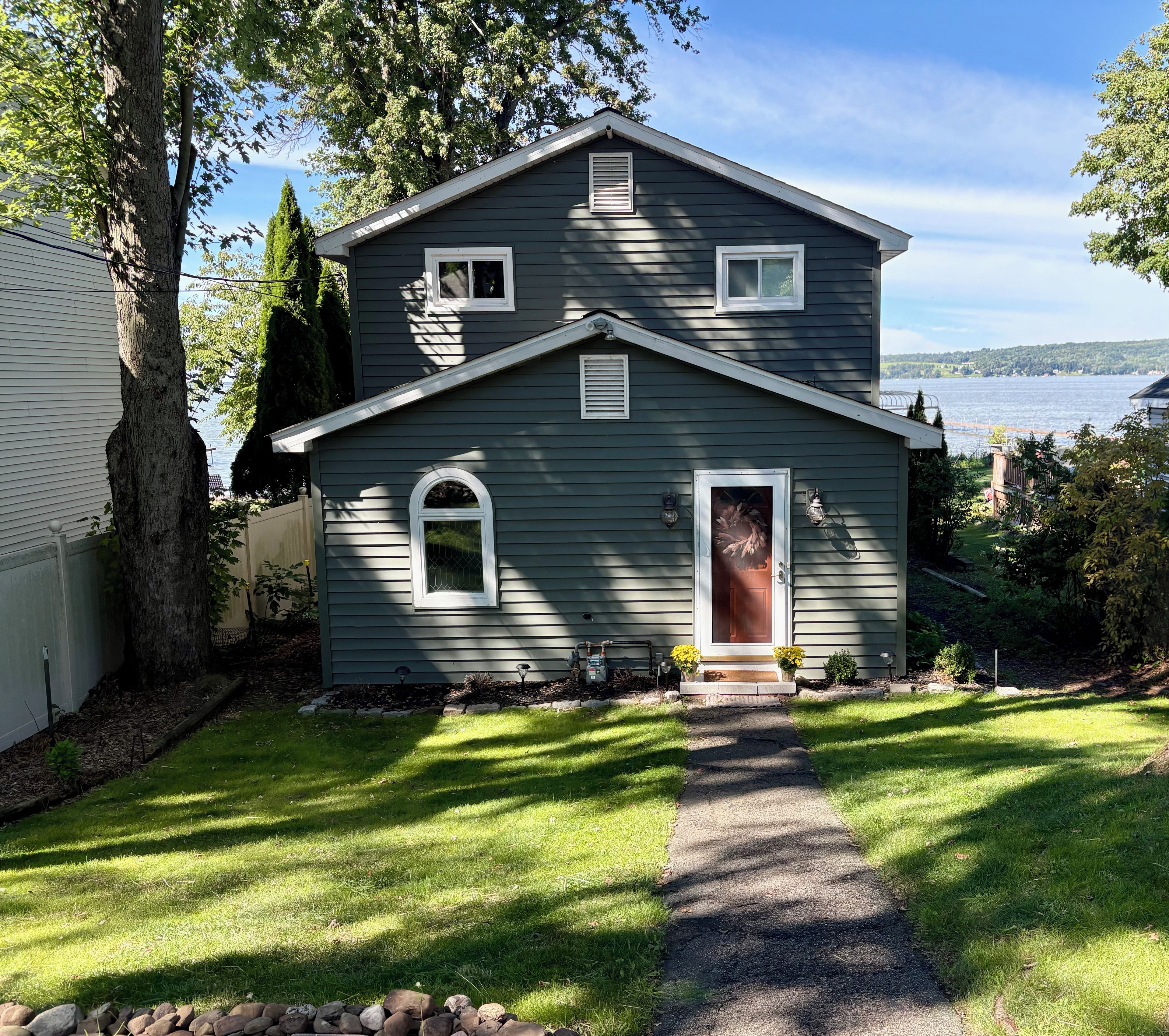 A two-story house with a front door, a small porch, and a view of a body of water.