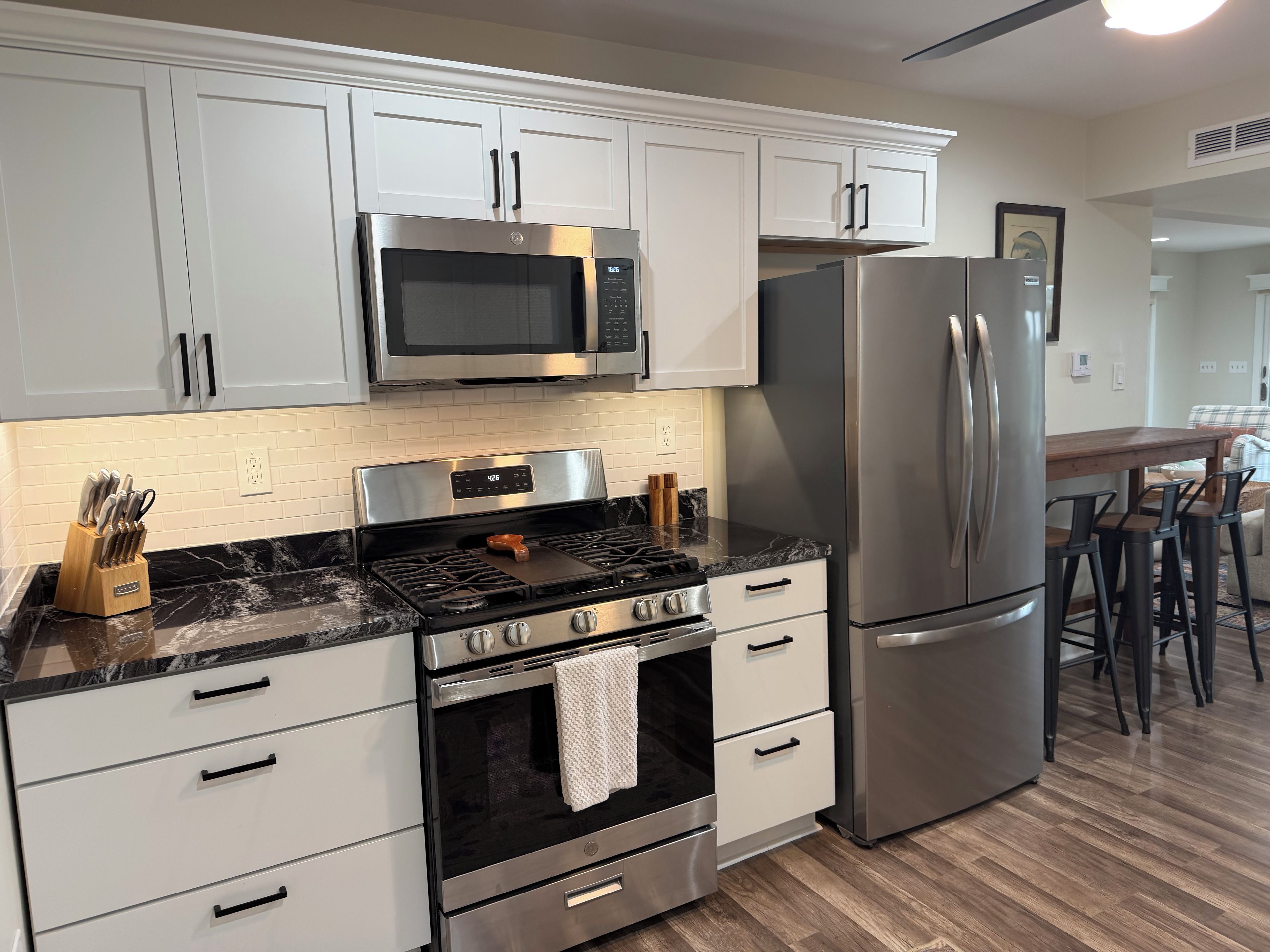 A modern kitchen with stainless steel appliances, white cabinetry, and a marble countertop.