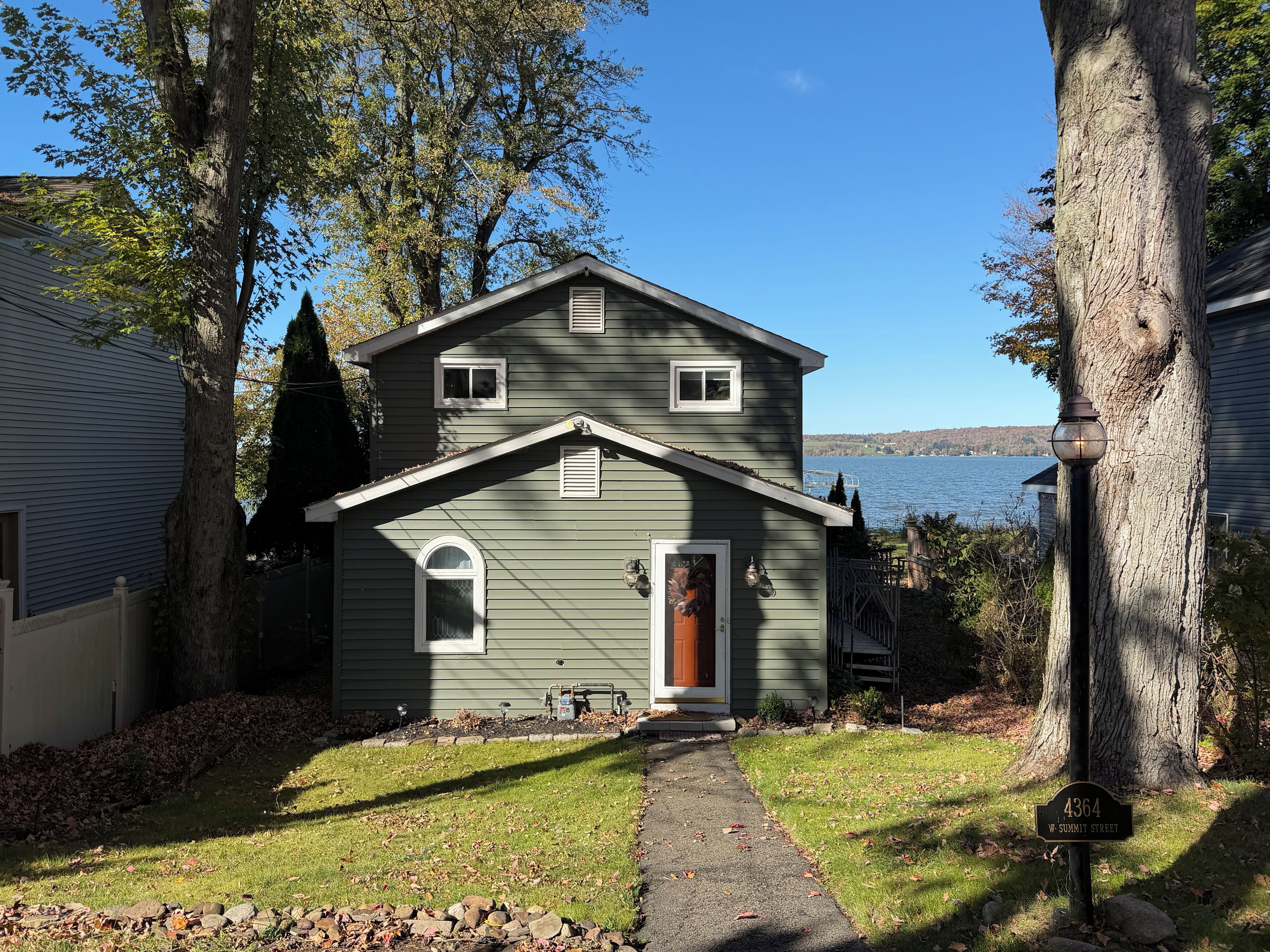 A two-story house with a front porch, a visible mailbox, and a clear view of a lake.