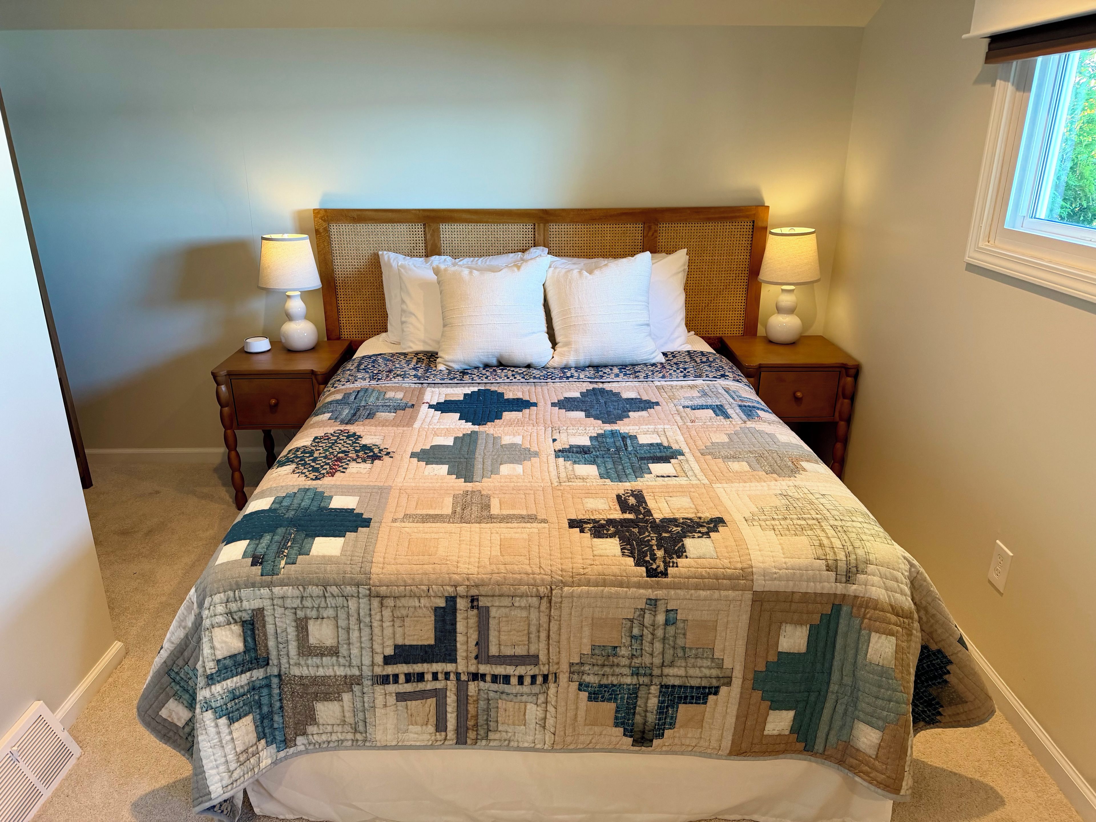 A bedroom with a large bed, two bedside tables, a window, and a wall vent.