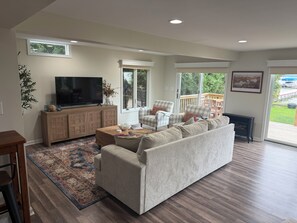 A living room with a large sofa, a television, and a wooden cabinet. - Welcoming 2-bedroom home on the shores of Lake Chautauqua (Lakewood)