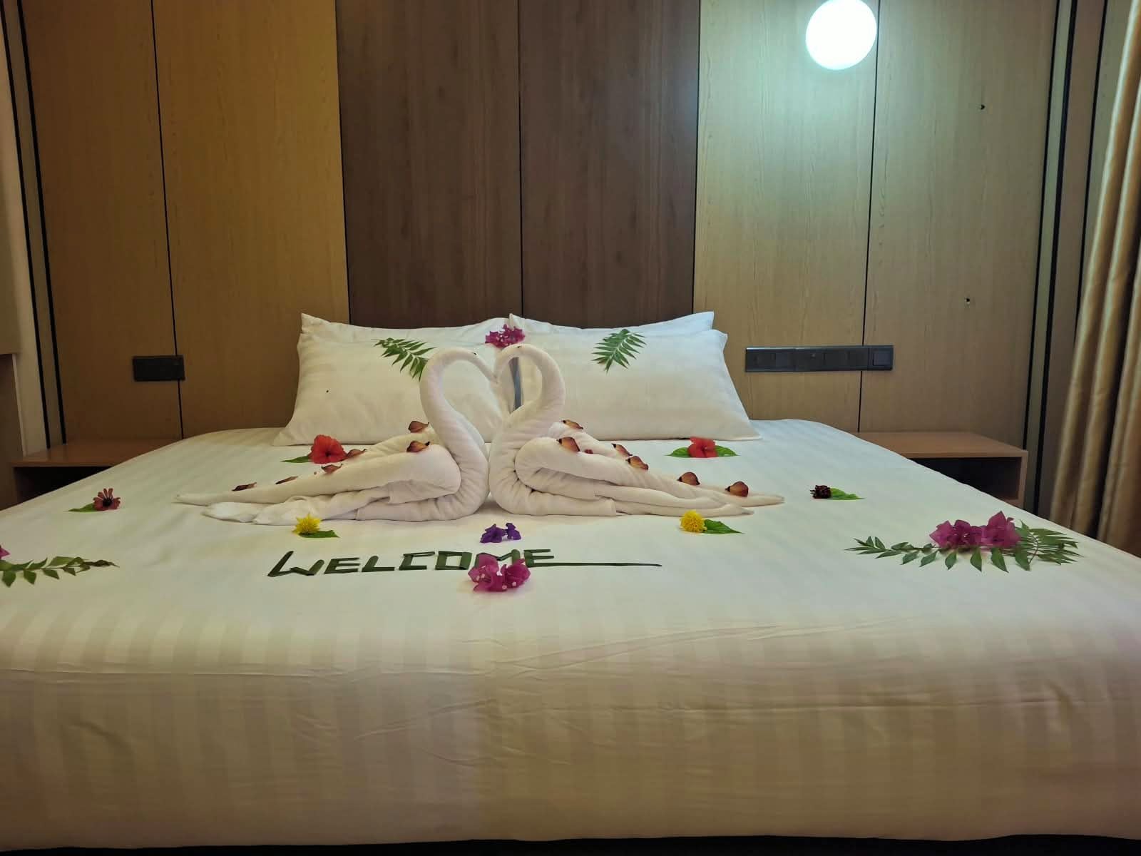 A hotel room with a neatly made bed, a welcome mat, and a wooden headboard.