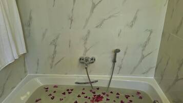 A bathroom with a bathtub filled with rose petals, a showerhead, and a towel hanging on the wall.
