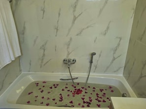 Ein Badezimmer mit einer Badewanne, gefüllt mit Rosenblättern, einer Duschbrause und einem Handtuch, das an der Wand hängt.