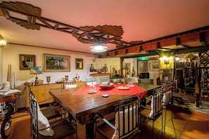 A dining area with a wooden table, chairs, and a red table runner. There are paintings on the walls and a ceiling fan above. - Villa Karusos , Pelion (Pelion)