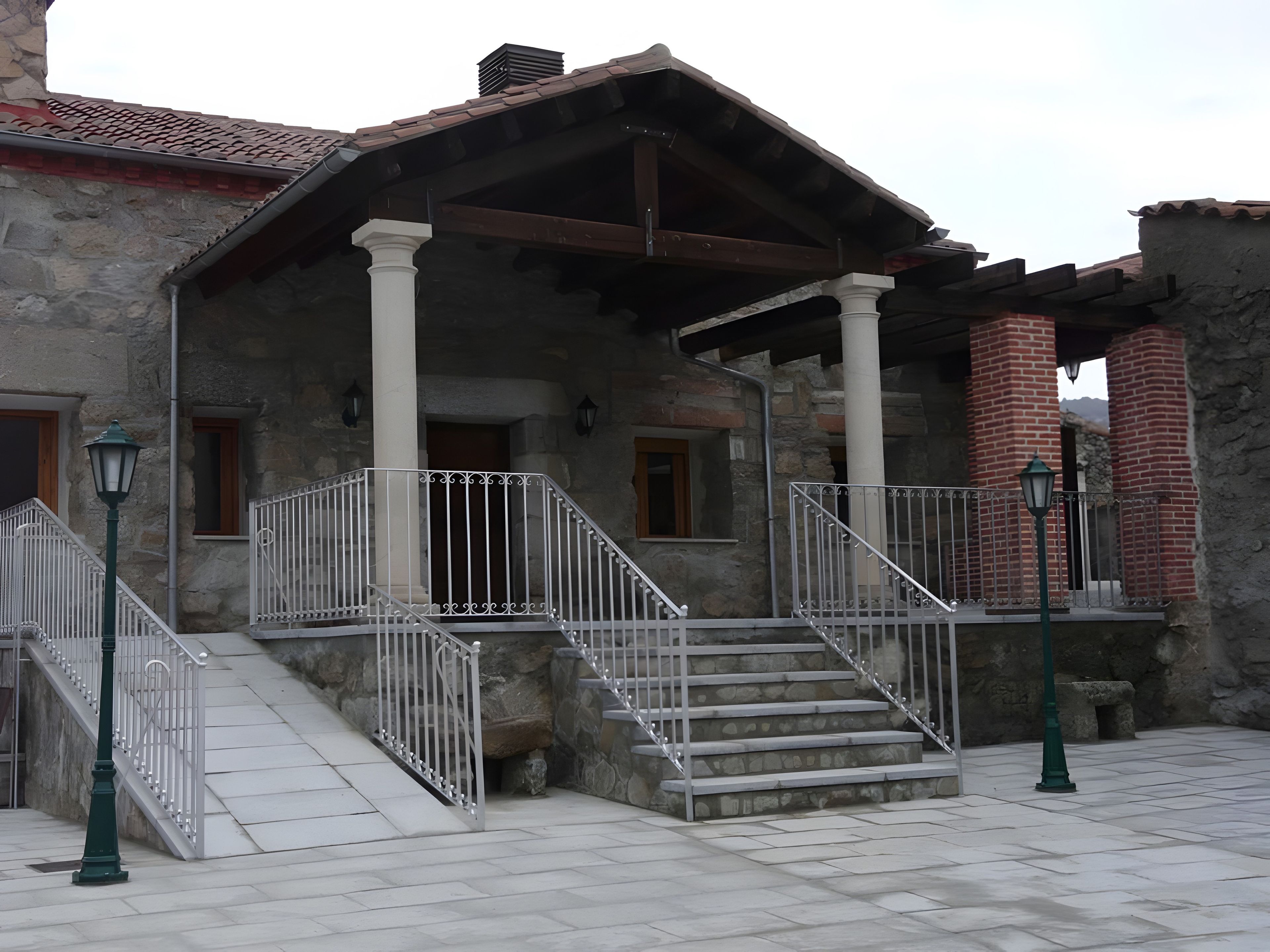 Un edificio in pietra con un portico coperto, una scala e un camino in mattoni.