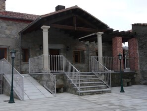 A stone building with a covered porch, a staircase, and a brick chimney. - Country House 'Casa Rural La Huerta Condesa' with Private Pool (Riofrío)