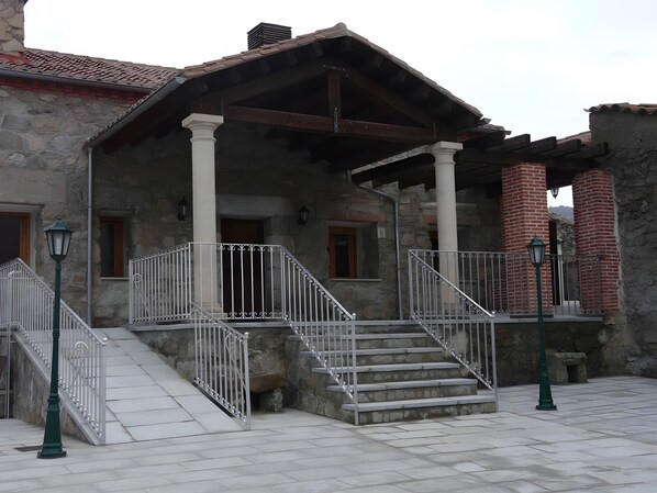A stone building with a covered porch, a staircase, and a brick chimney.
