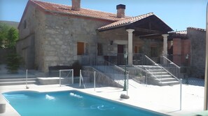 A stone building with a swimming pool, outdoor stairs, and a covered area.