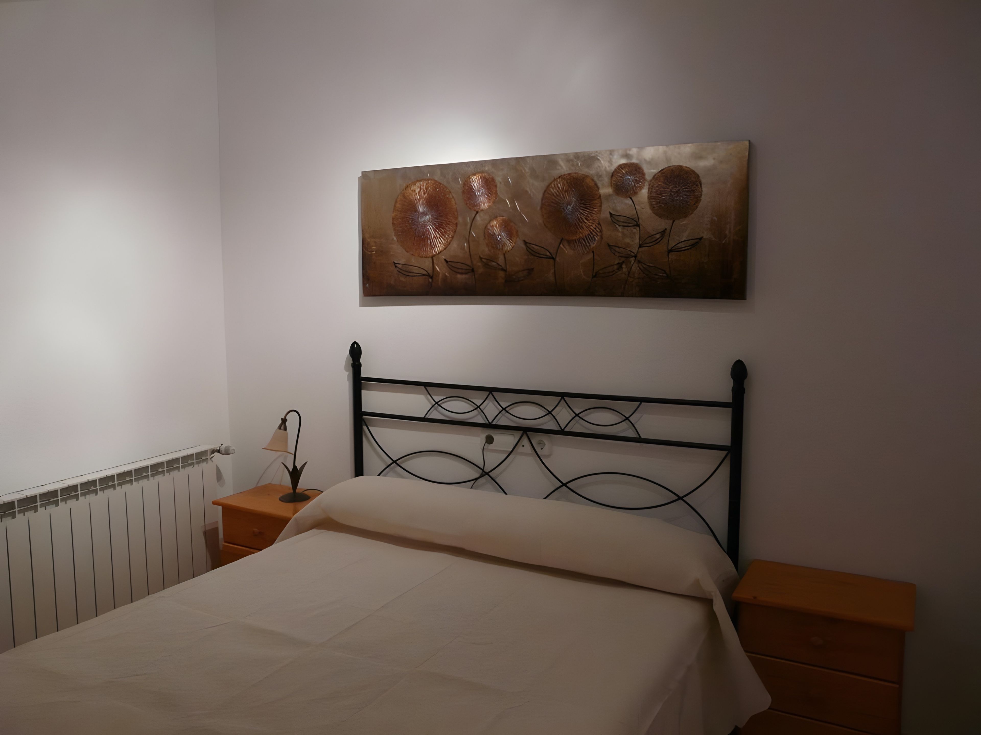 Quarto com cama, mesa de cabeceira, obra de arte na parede e radiador.