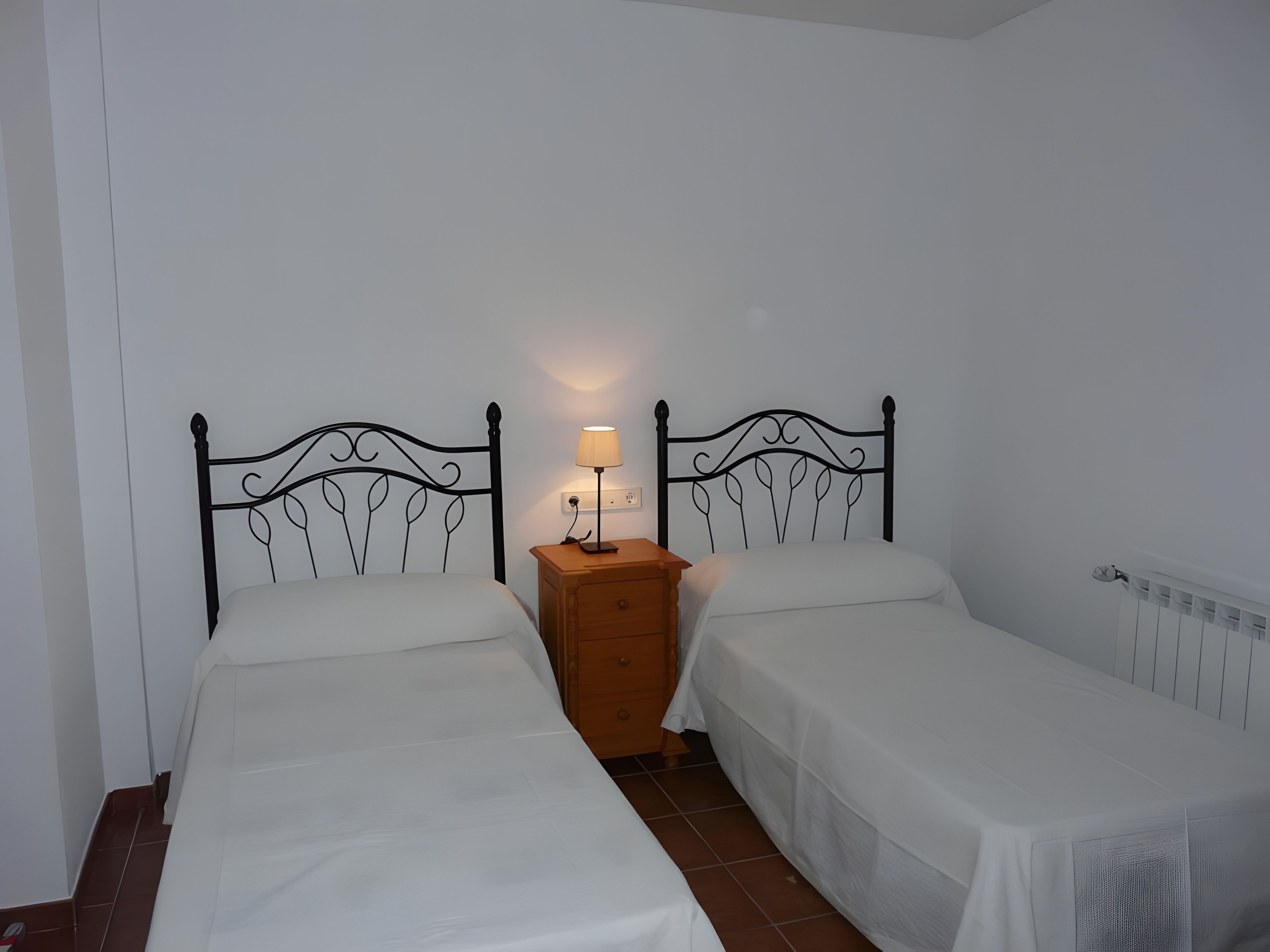 A twin room with two single beds, a wooden nightstand with a lamp, and a white radiator.