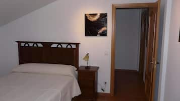 A bedroom with a bed, a nightstand, a wall-mounted lamp, and a door leading to another room.